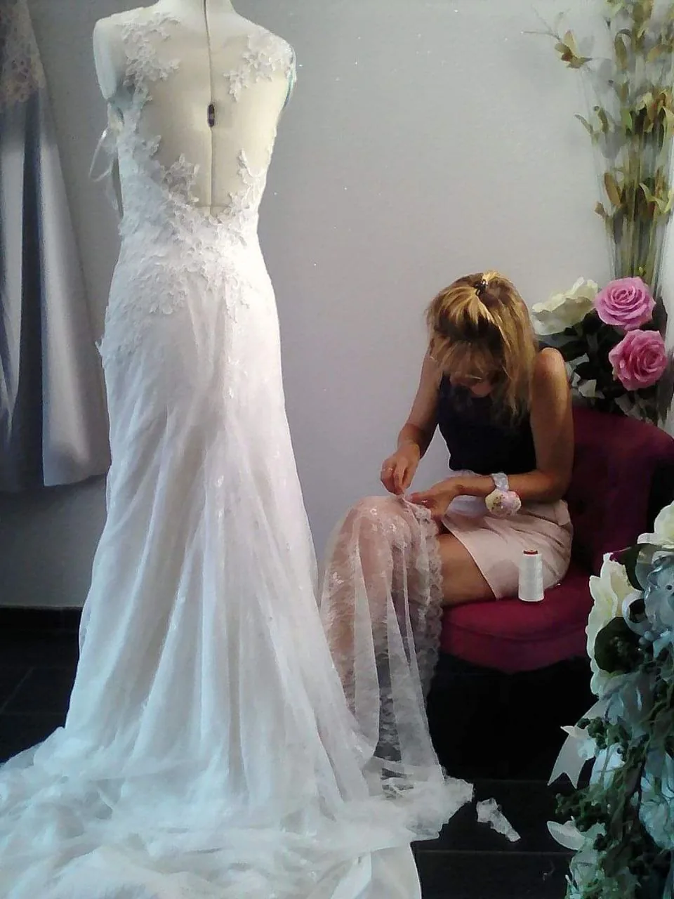 Atelier de couture : robe de mariée de dos sur mannequin, couturière travaillant la dentelle