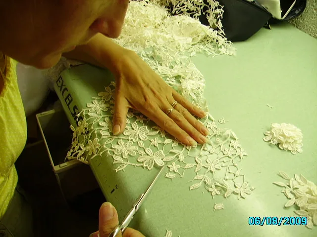 Atelier : découpe de motifs de dentelle florale sur tulle blanc posé sur la table de travail.