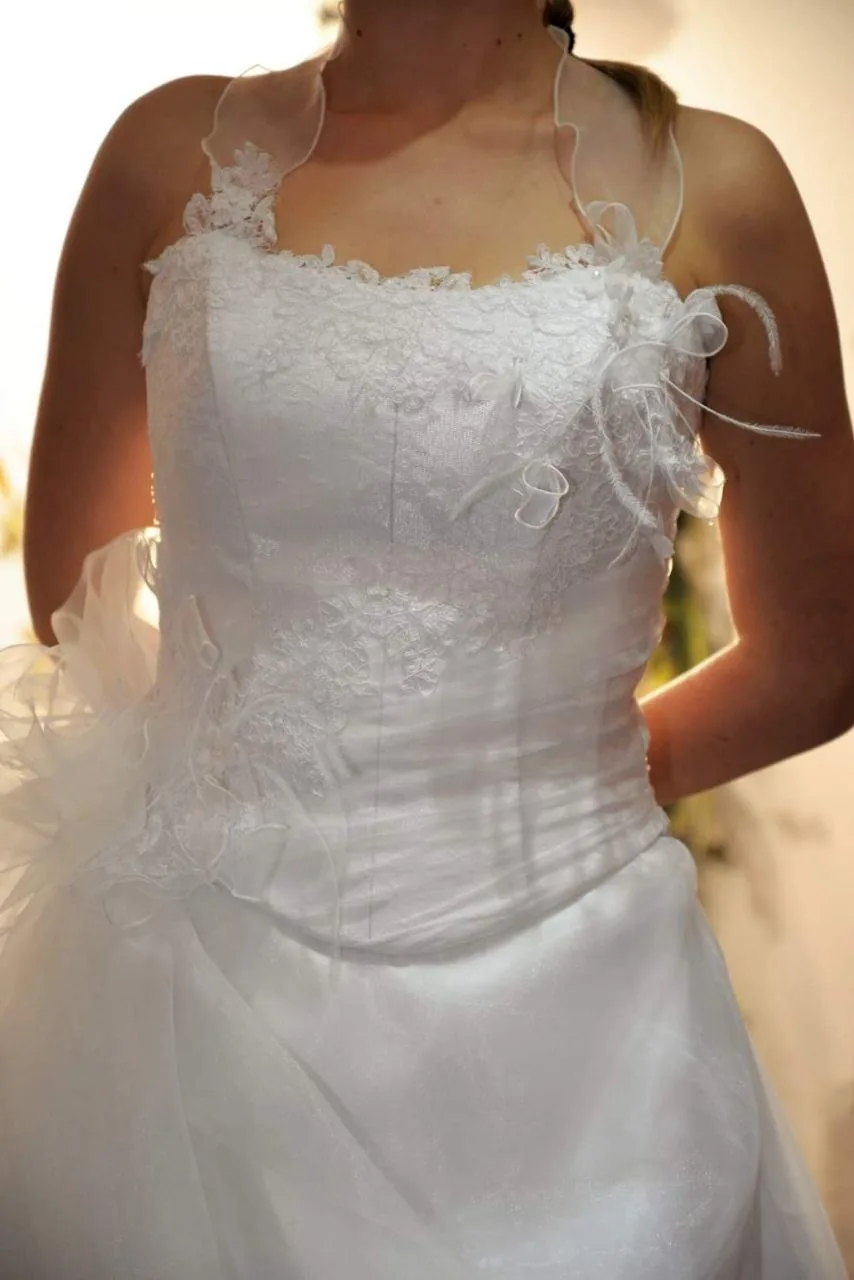 Détail du buste d'une robe de mariée en dentelle florale, fines bretelles et nœud de tulle à la taille