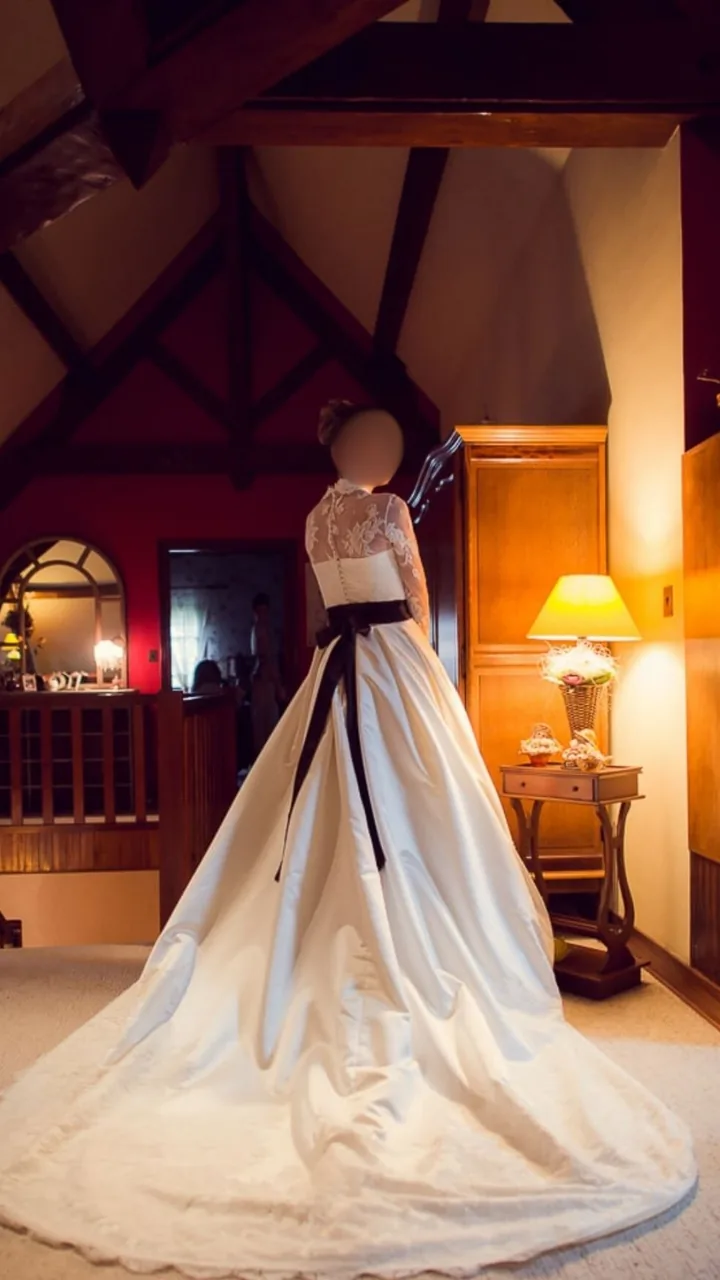 Dos d'une robe ivoire en dentelle à col montant, ceinture ruban noir nouée et longue traîne satinée.