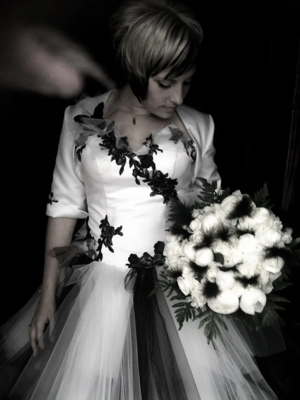 Photo noir et blanc d'une robe blanche à dentelle noire, boléro et ceinture noire, bouquet blanc.