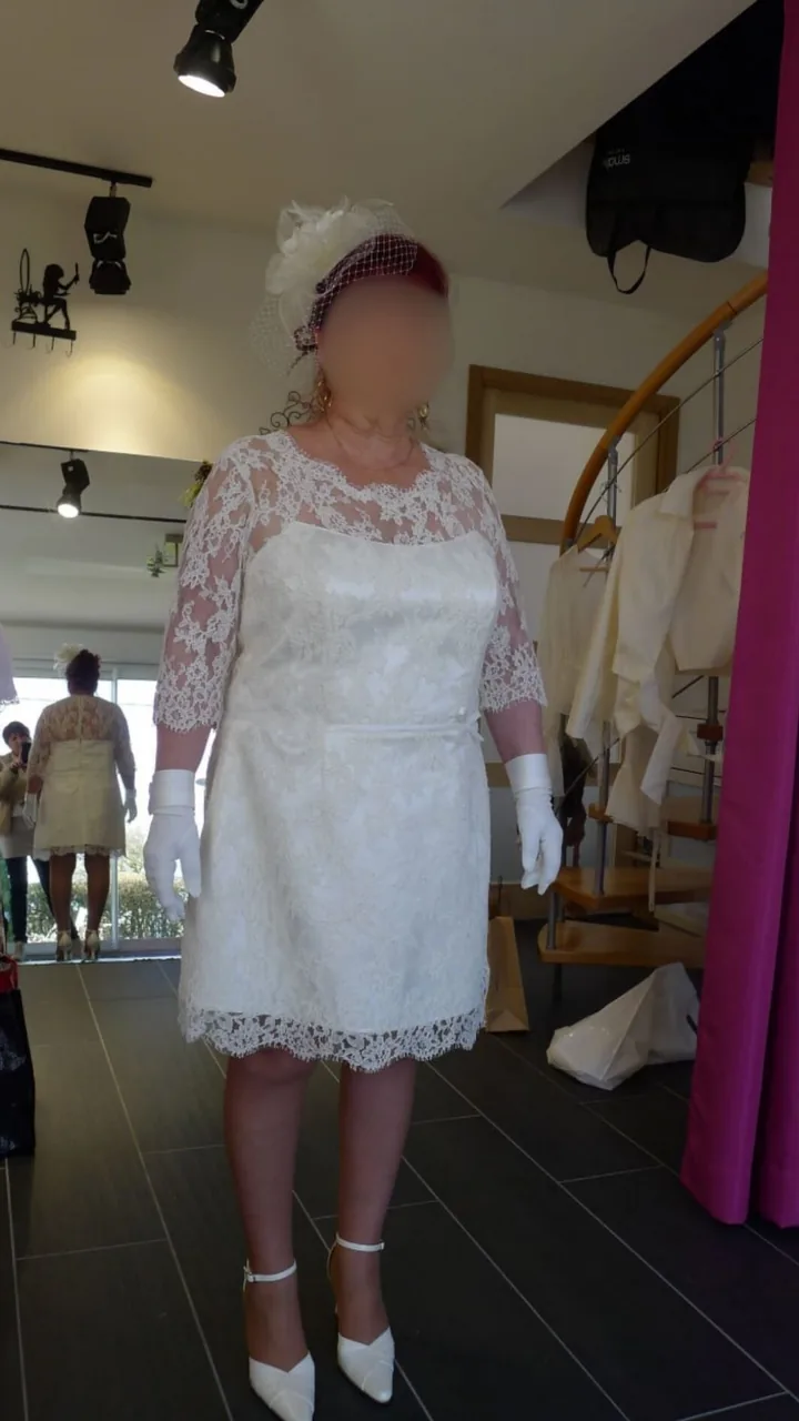 Robe de mariée courte en dentelle florale : manches 3/4, ceinture fine à nœud et voilette, portée en boutique
