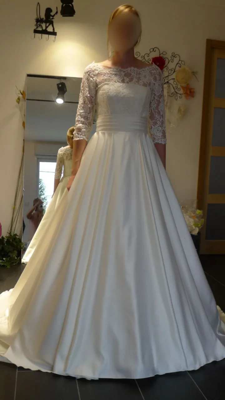Robe de mariée ligne A en dentelle : manches longues, large ceinture plissée et jupe satin devant le miroir