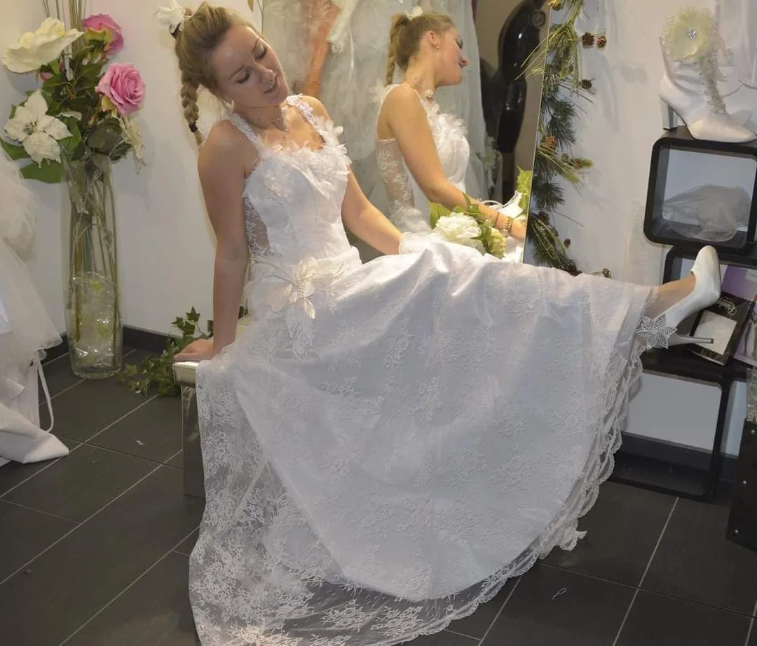 Femme en robe de mariée en dentelle assise en boutique lors d'un essayage, jupe évasée à bord festonné