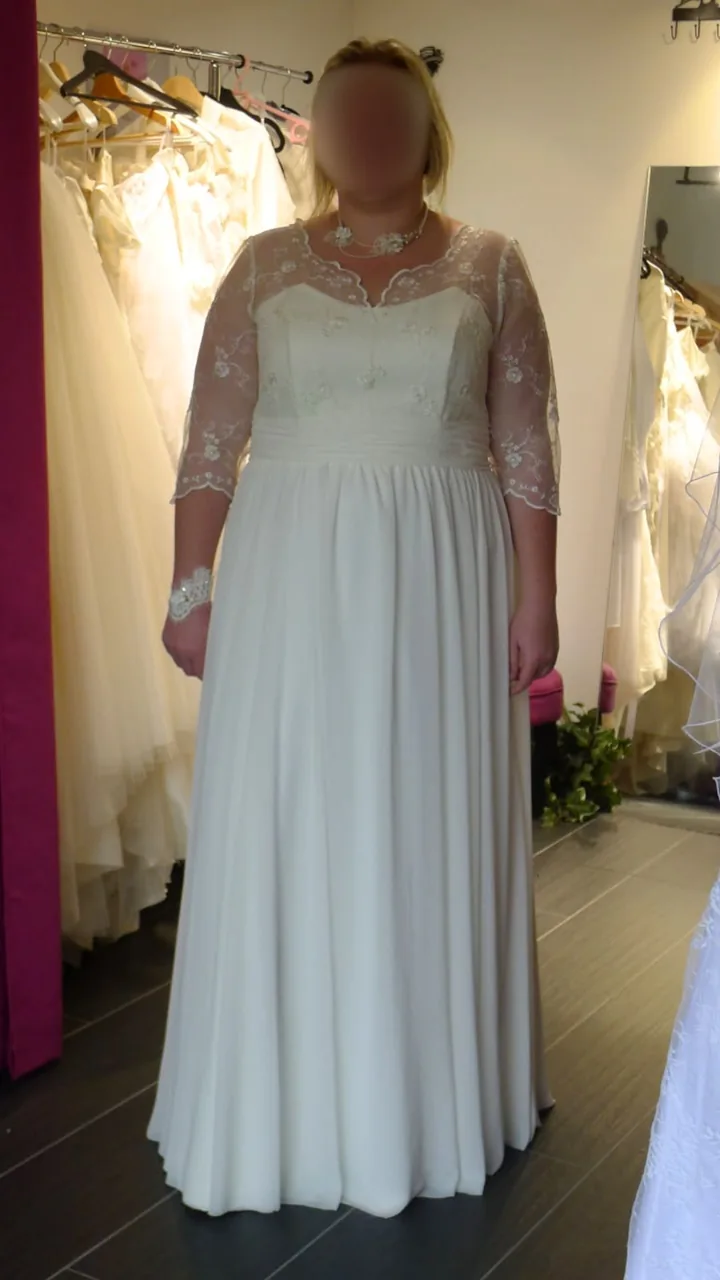 Robe de mariée ligne A en dentelle fleurie : manches trois-quarts, encolure illusion et ceinture plissée