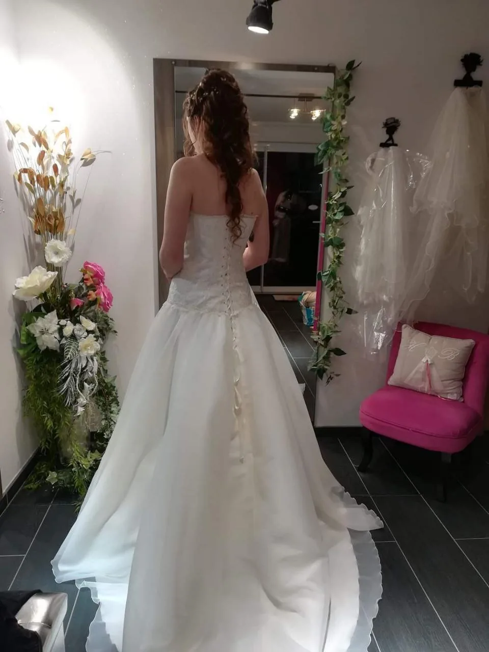 Robe de mariée princesse en tulle et dentelle, dos boutonné et traîne, portée de dos devant un miroir