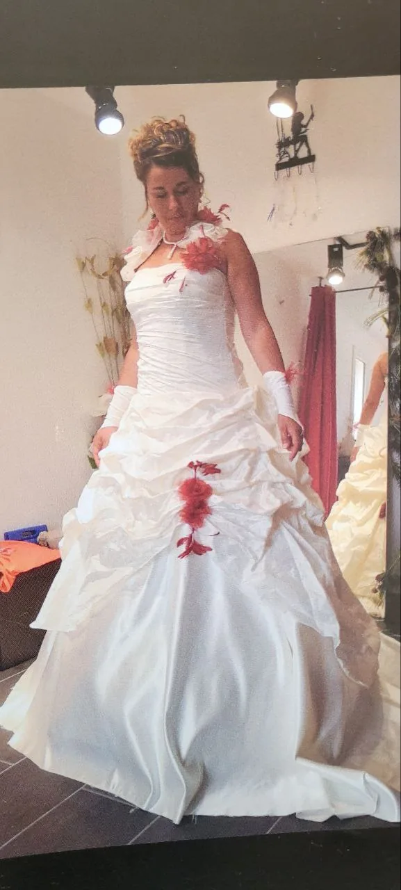 Robe de mariée blanche à corsage froncé, fleurs rouges en tissu et jupe à volants superposés