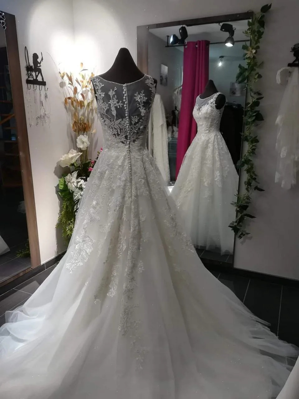 Robe de mariée ligne A en tulle couvert de dentelle florale appliquée, dos boutonné et longue traîne sur buste