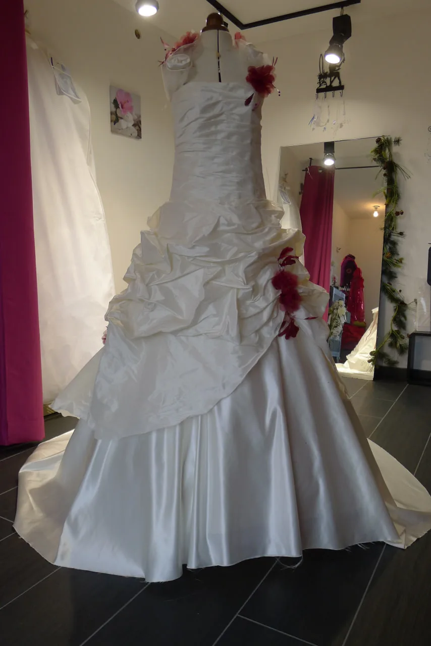 Robe de mariée ivoire en satin sur mannequin, drapé asymétrique à la taille et ornements rose bordeaux.