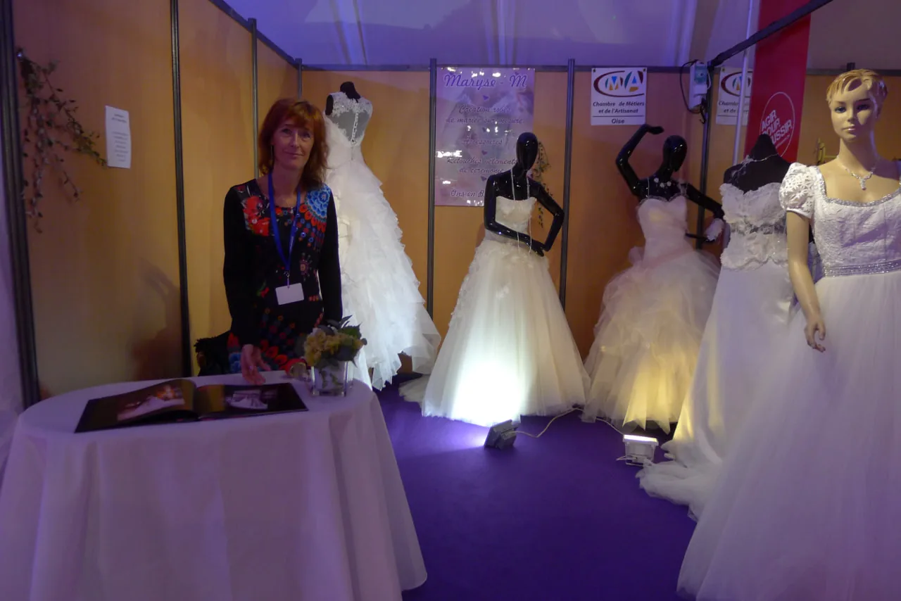 Robes de mariée blanches sur mannequins à un stand de salon, bustes en dentelle et jupes en tulle.